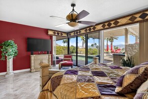A bedroom with a large bed, a television, a potted plant, and a view of a pool and outdoor seating area. - Stunning vacation rental in the prestigious Mirage Cove gated community. (Rancho Mirage)