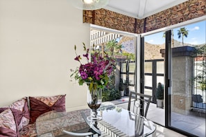 A room with a glass table, a vase with purple flowers, a patterned sofa, and a view of a garden and mountains. - Stunning vacation rental in the prestigious Mirage Cove gated community. (Rancho Mirage)