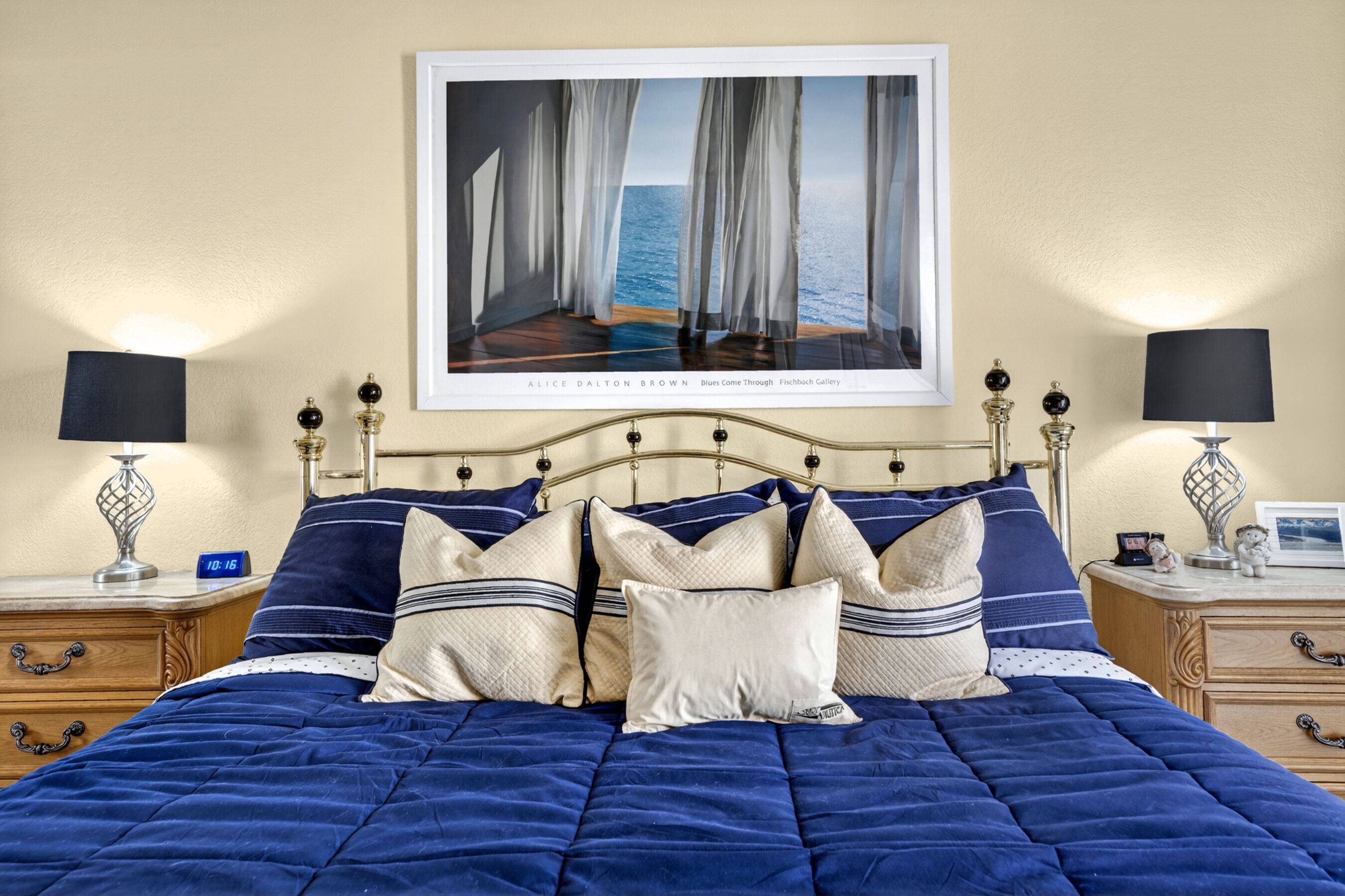 A hotel room with a bed, two bedside tables, a nightstand, a framed picture on the wall, and a clock.