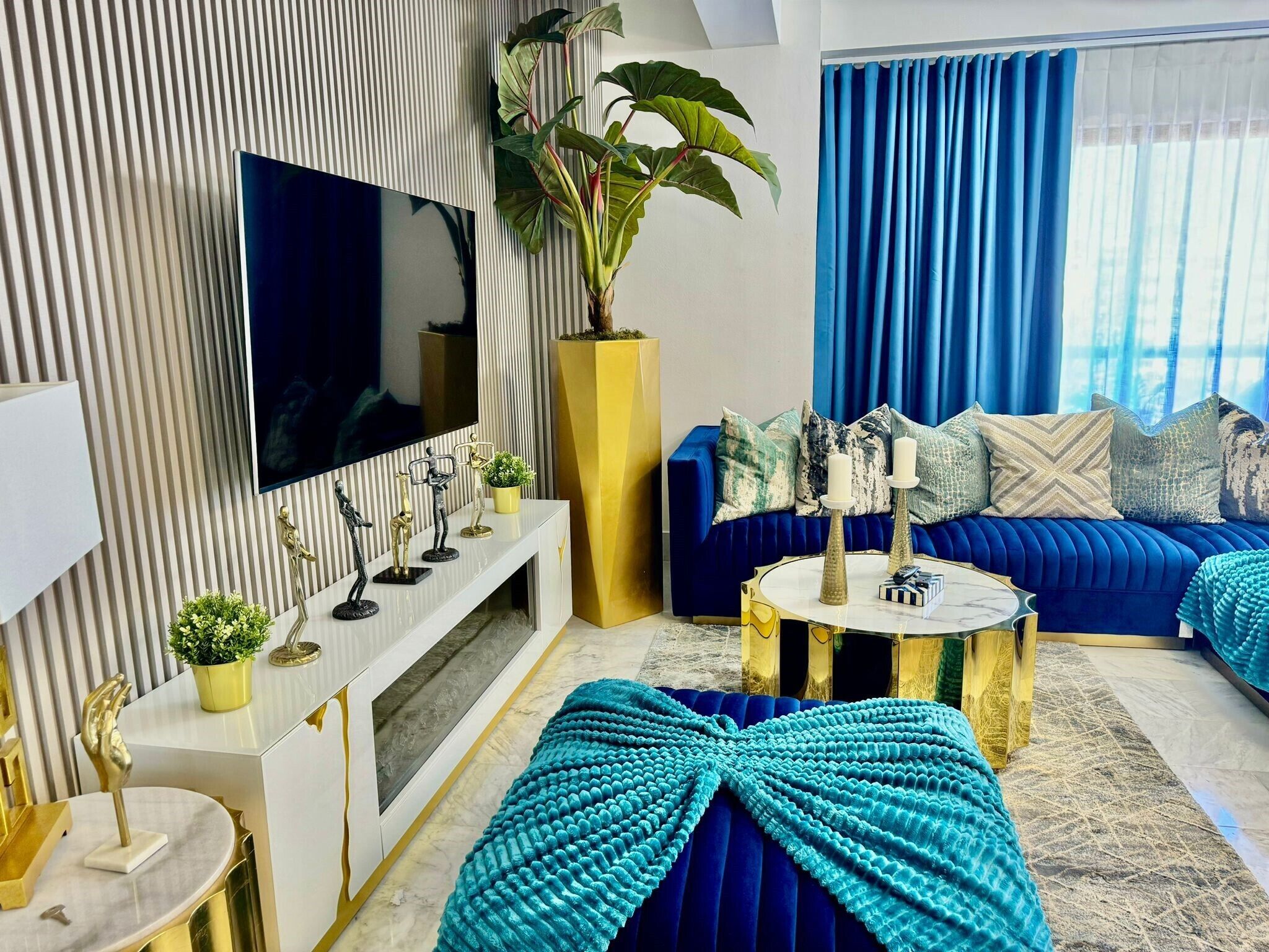 Una sala de estar moderna con un televisor de pantalla plana grande, un sofá azul y una planta decorativa.