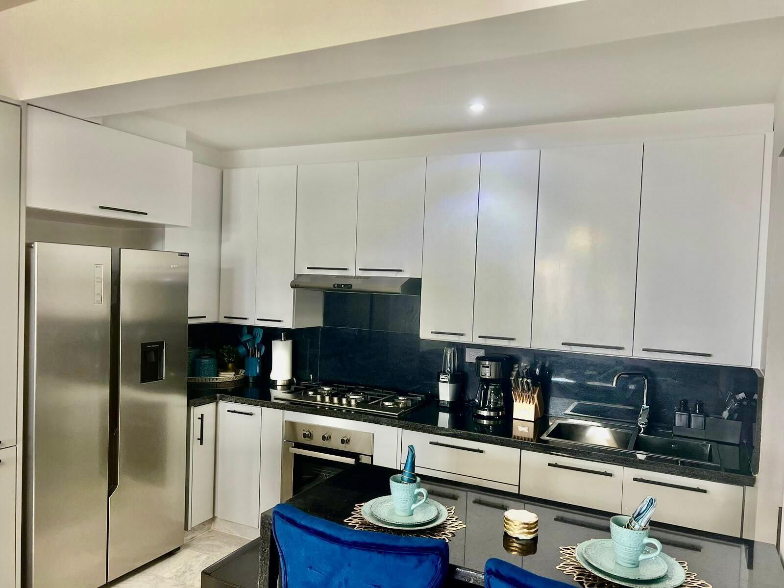 A modern kitchen with white cabinets, stainless steel appliances, and a black countertop.