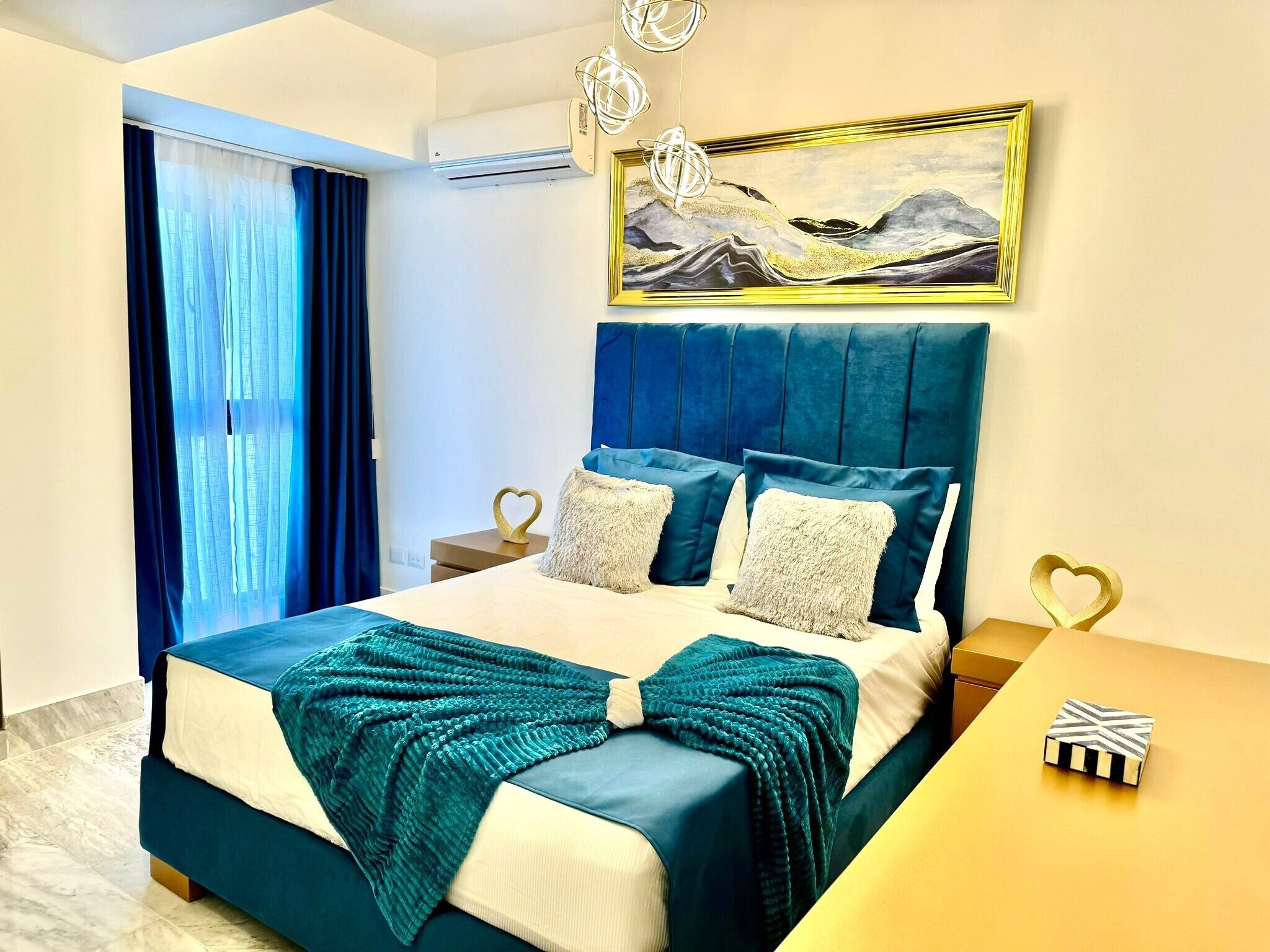 Habitación de hotel con cama, un cuadro, una mesa y ventana con cortinas.