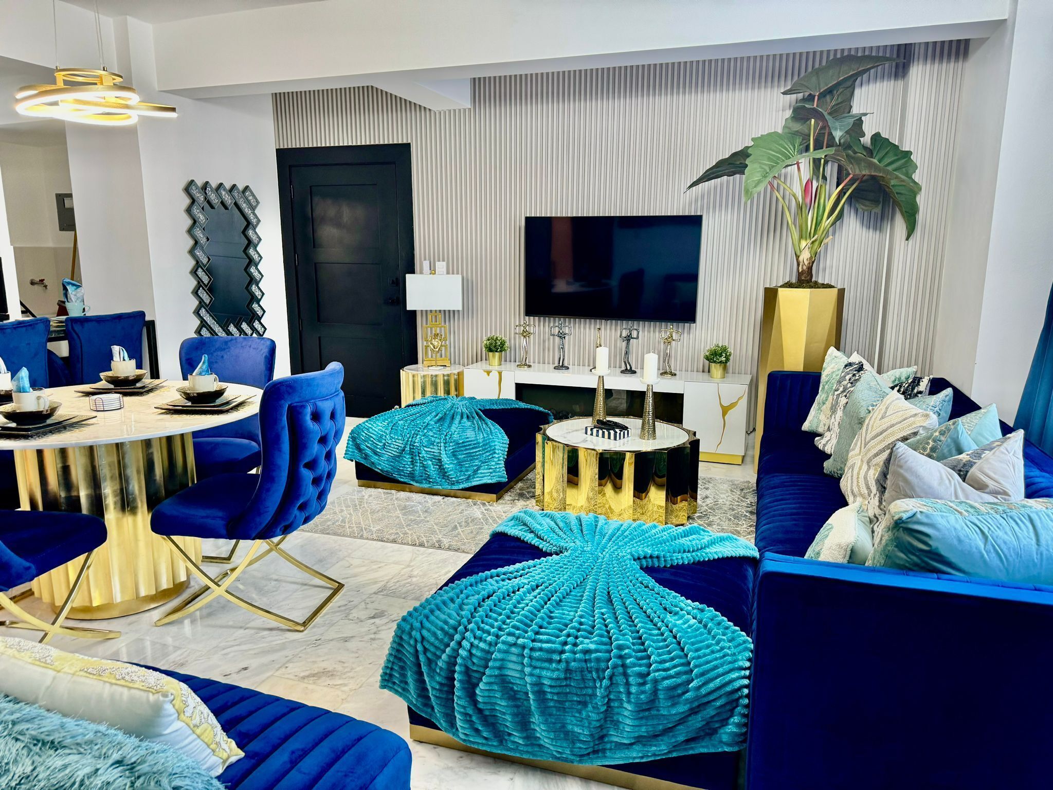 Un salon moderne avec une table ronde, des fauteuils bleus, un canapé et un téléviseur fixé au mur.