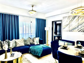 A modern living room with a blue sofa, a round coffee table, and a dining area with a chair and table. - Luxury Tower Apartment Near Monument  Pool & Balcony (Santiago de los Caballeros)