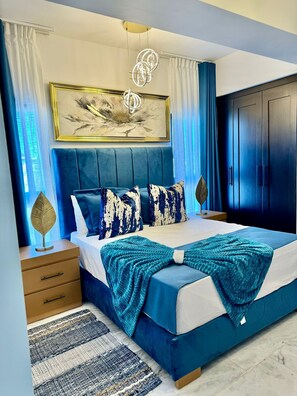 Ein Schlafzimmer mit einem großen Bett, einem Kopfteil, einem Nachttisch, einer Stehlampe, einem Gemälde und einem Kleiderschrank.