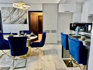A modern kitchen with white cabinets, a marble backsplash, and a dining area with blue velvet chairs and gold accents. - Luxury Tower Apartment Near Monument  Pool & Balcony (Santiago de los Caballeros)