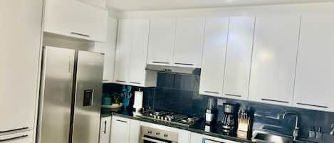 Una cocina moderna con armarios blancos, electrodomésticos de acero inoxidable y encimera negra.