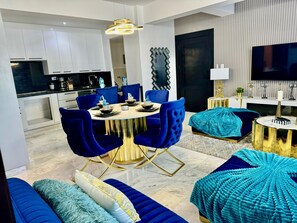 Ein modernes Wohnzimmer mit Essbereich, mit einem runden Tisch, blauen Polsterstühlen und einem Sofa mit Strukturmuster.