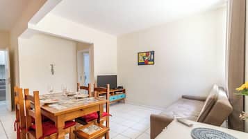 A dining area with a wooden table set for four, a sofa, and a TV stand with a television.