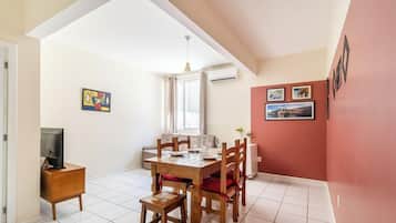 A dining area with a wooden table and chairs, a television on a stand, and artwork on the walls.