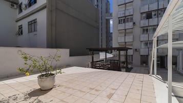 A rooftop terrace with tiled flooring, a potted plant, and a wooden pergola.