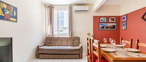 A compact living space with a sofa, dining table, chairs, and artwork on the walls.