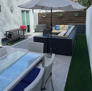 Eine Terrassenanlage mit einem Tisch mit Glasplatte, Korbstühlen, einer Couch und einem Deckenventilator.