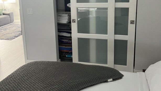 A bedroom with a bed, a wardrobe with glass doors, and a visible closet with folded clothes. - Tranquil Retreat – 2 Bedroom Las Olas (Fort Lauderdale)
