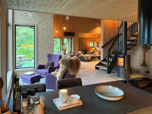 A cozy interior with a wooden ceiling, a fireplace, a dining area, and a view of greenery outside.