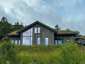 Une maison moderne en bois, dotée de grandes fenêtres et d’un toit à pente.