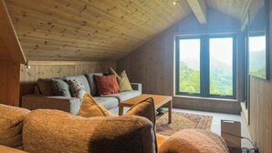 A cozy room with a sloped ceiling, a sofa with cushions, a coffee table, and a large window offering a view of the outdoors. - Mountain cabin in Ljosland with ski-in access (Åseral)