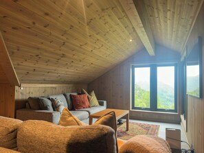 A cozy room with a sloped ceiling, a sofa with cushions, a coffee table, and a large window offering a view of the outdoors. - Mountain cabin in Ljosland with ski-in access (Åseral)
