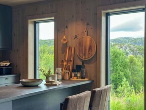 A kitchen with wooden walls, a window overlooking greenery, and a rustic wooden spoon rack.