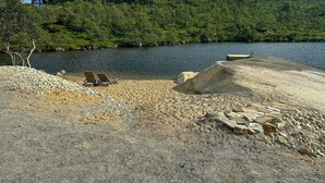 A beach with two lounge chairs, a rocky area, and a body of water with hills in the background. - Mountain cabin in Ljosland with ski-in access (Åseral)