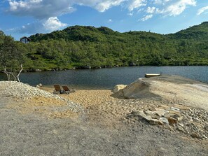 A beach with two lounge chairs, a rocky area, and a body of water with hills in the background. - Mountain cabin in Ljosland with ski-in access (Åseral)