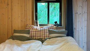 A bed with a white duvet and patterned pillows, a window with a view of greenery, and a desk with a lamp. - Mountain cabin in Ljosland with ski-in access (Åseral)