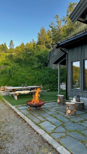 Une terrasse avec un foyer, une table et des chaises, et une structure en bois dotée de fenêtres.