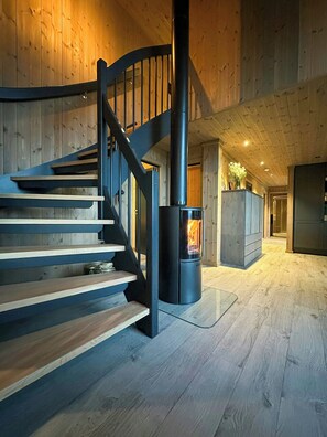 A wooden staircase with a black railing leading to a room with a wood-burning stove.