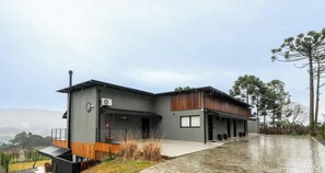 A modern two-story building with a flat roof, a covered outdoor area, and a paved driveway.