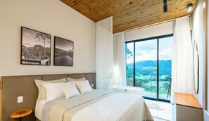 A bedroom with a large bed, a view of a landscape through a window, and two framed pictures on the wall.