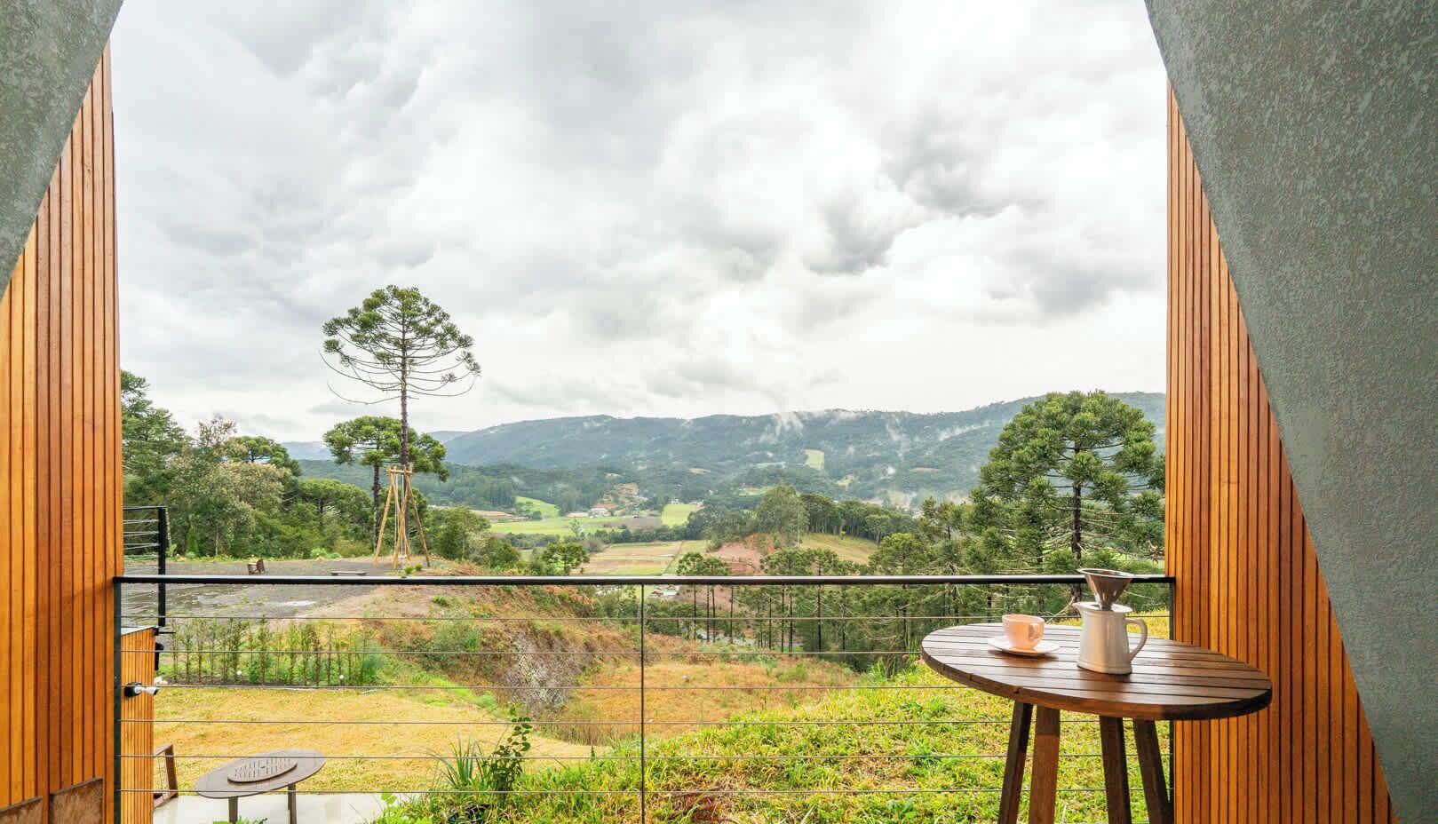 A balcony with a table and chairs, overlooking a scenic landscape with trees and hills.