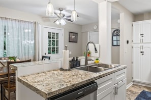 Cocina con encimeras de granito, lavavajillas, pileta y ventilador de techo.