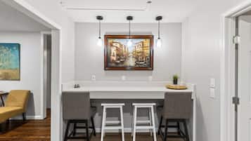 A kitchen with a white countertop, two bar stools, a painting above the counter, and pendant lights.