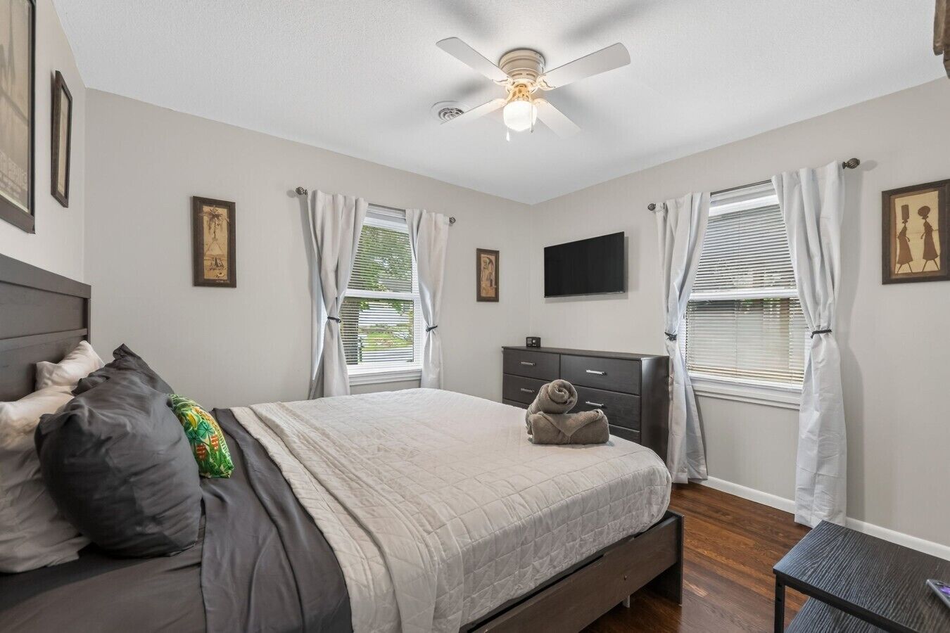 A bedroom with a bed, a ceiling fan, a dresser, and a TV on the wall.
