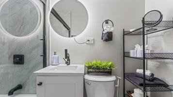 A modern bathroom with a marble shower, a sink with a mirror, a toilet, and a shelf with toiletries.
