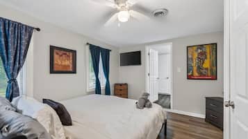Ein Schlafzimmer mit einem Bett, einem Deckenventilator, einem Fernseher und Kunstwerken an den Wänden.