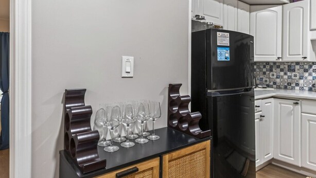 A kitchen with a black refrigerator, white cabinets, a clock on the wall, and a wine rack with glasses. - 3 bdrm, 7 Minutes from downtown (Kansas City)