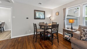 A dining area with a wooden table and chairs, a framed artwork on the wall, and a window with blinds. - 3 bdrm, 7 Minutes from downtown (Kansas City)