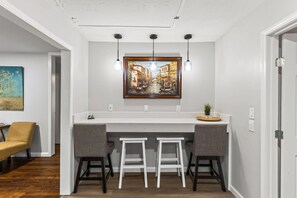 A kitchen with a white countertop, two bar stools, a painting above the counter, and pendant lights.
