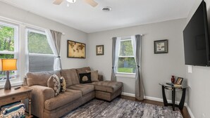 A living room with a sectional sofa, a ceiling fan, a flat-screen TV, and two windows with curtains. - 3 bdrm, 7 Minutes from downtown (Kansas City)