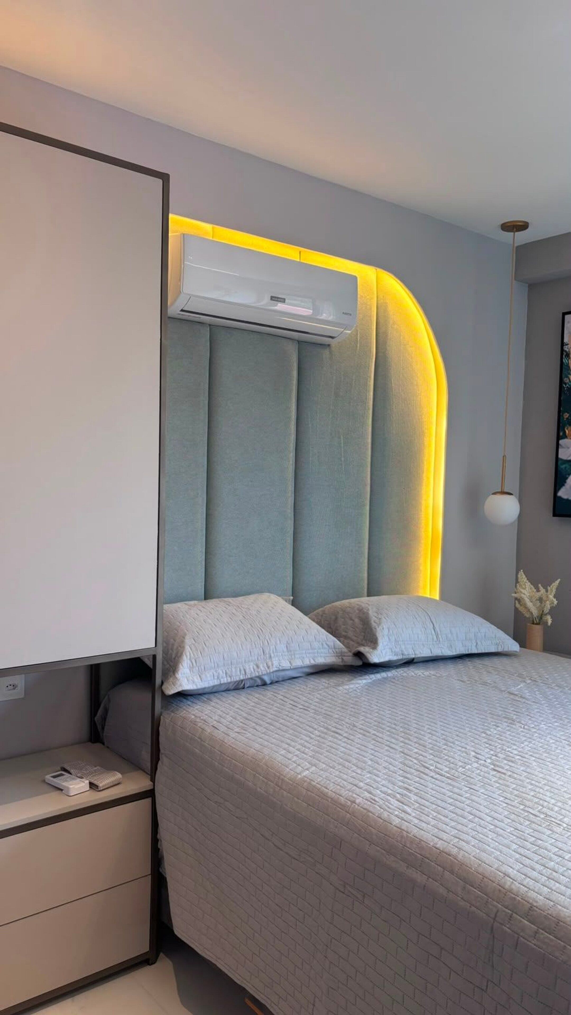 A modern bedroom with a bed, bedside tables, and an air conditioning unit.