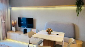 Una sala de estar moderna con una televisión de pantalla plana, un sofá, una mesa de comedor con sillas y una pequeña planta en maceta.