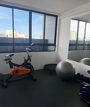 Un gimnasio con equipo de ejercicio, un amplio ventanal y vistas a edificios.