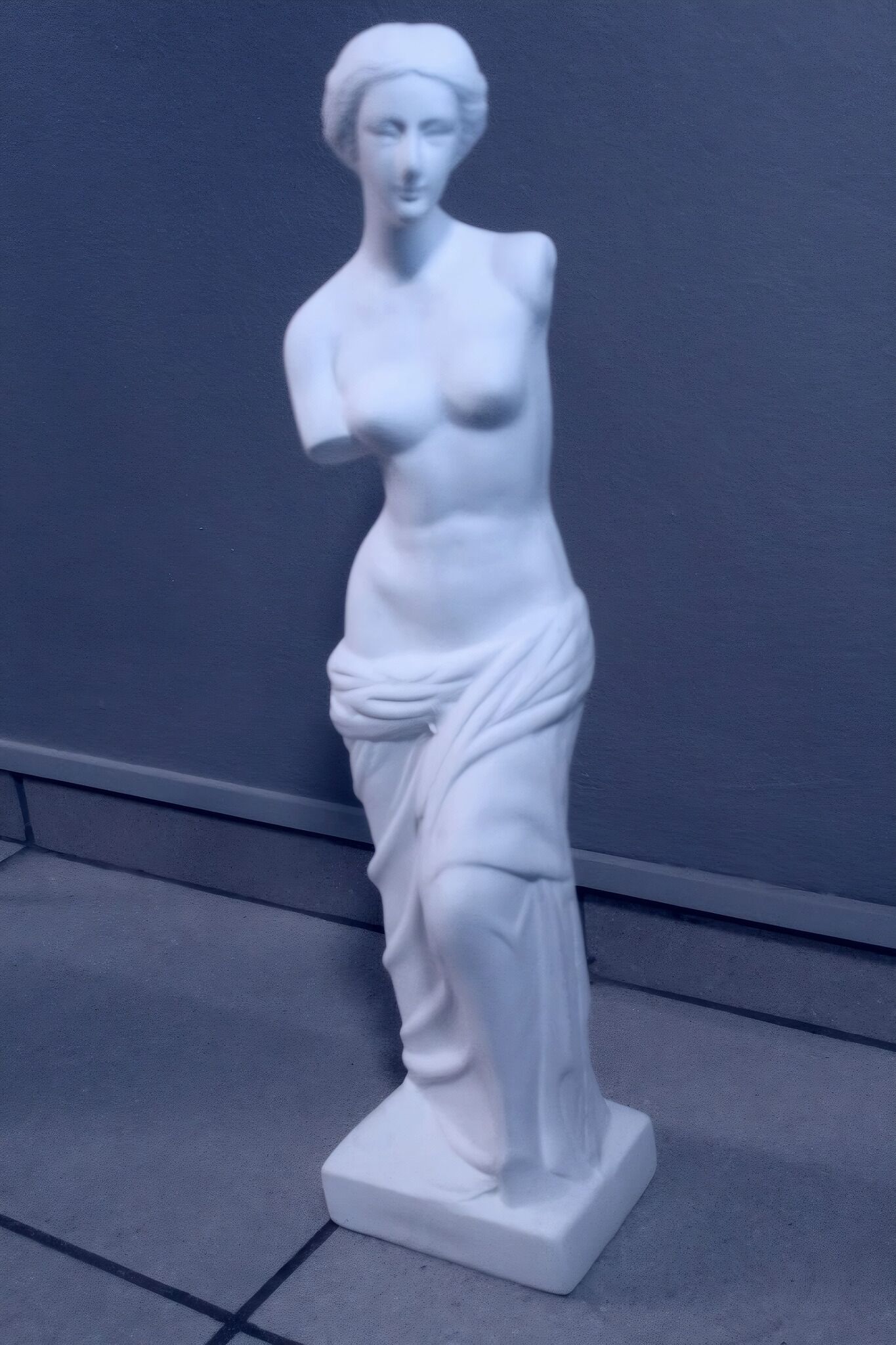 A white statue of a figure with a draped garment, standing on a pedestal.