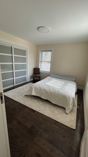 Un dormitorio con una cama, una silla, una ventana con persianas y un armario con puertas de vidrio esmerilado.