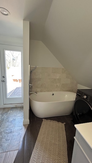 Un baño moderno con una bañera independiente, una lavadora y una puerta que da a un balcón.