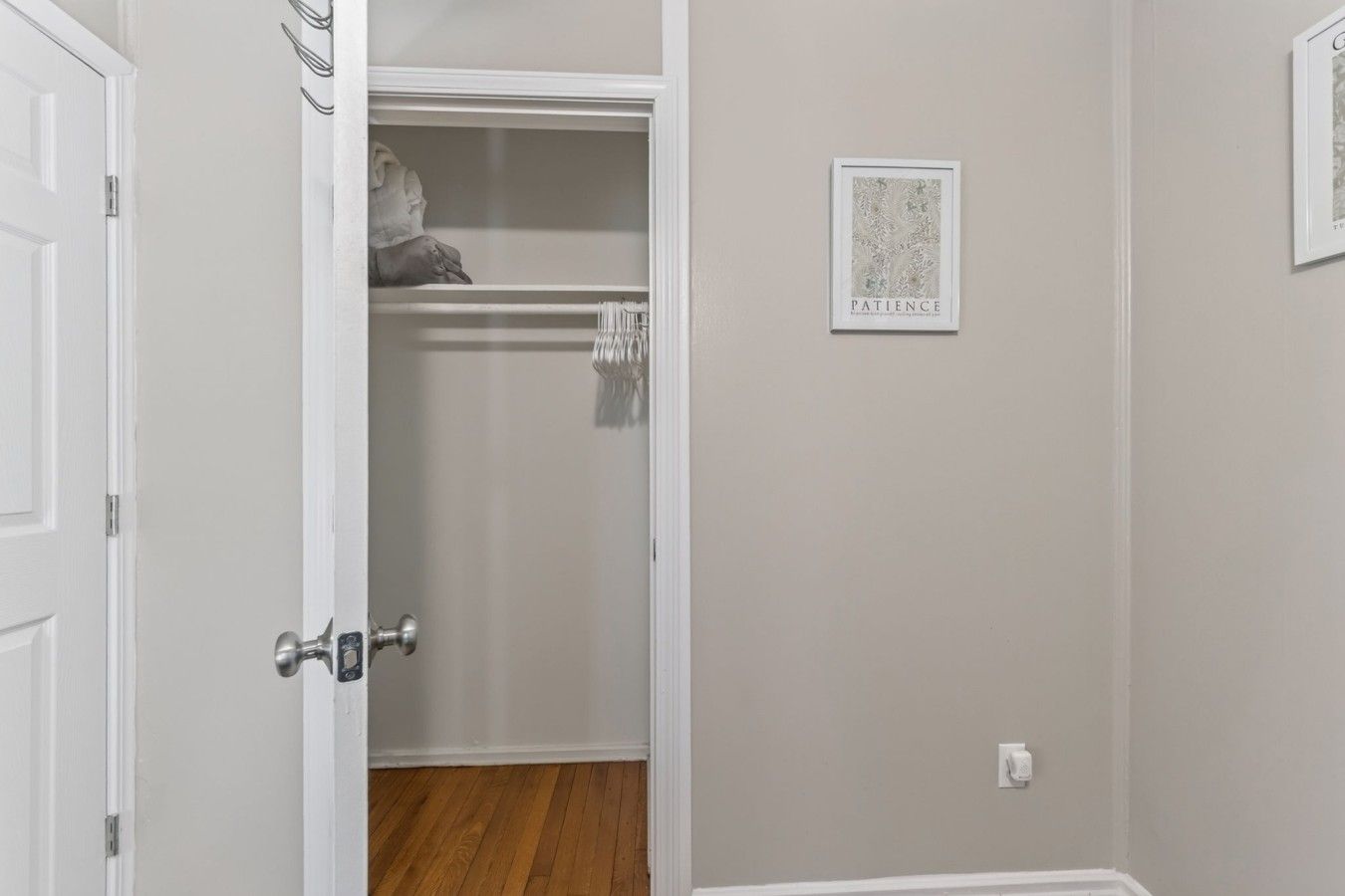 A room with a wooden floor, a white door, and a closet with hanging clothes.