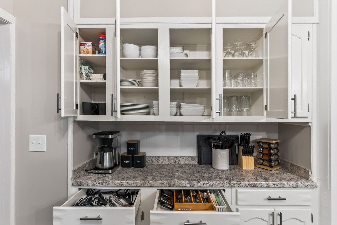 A kitchen with white cabinets, a coffee maker, and various kitchen utensils.