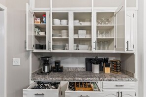 Una cocina con armarios blancos, una cafetera y diversos utensilios de cocina.