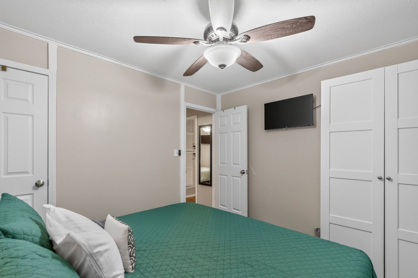 A bedroom with a bed, a ceiling fan, and white doors.